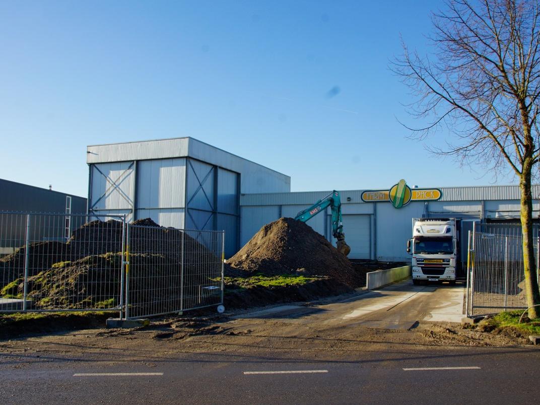 Gebouw Farm Pack met een graafmachine en bergen aarde voor de deur