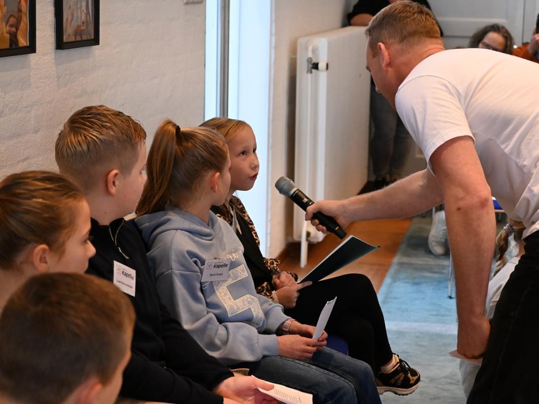 Presentator stelt vragen aan een meisje dat zit naast andere kinderen