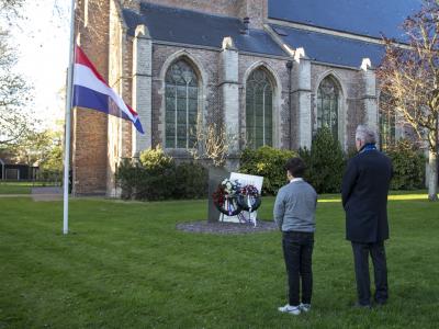 Burgemeester en kinderburgemeester staan voor kransen, vlag halfstok bij de kerk